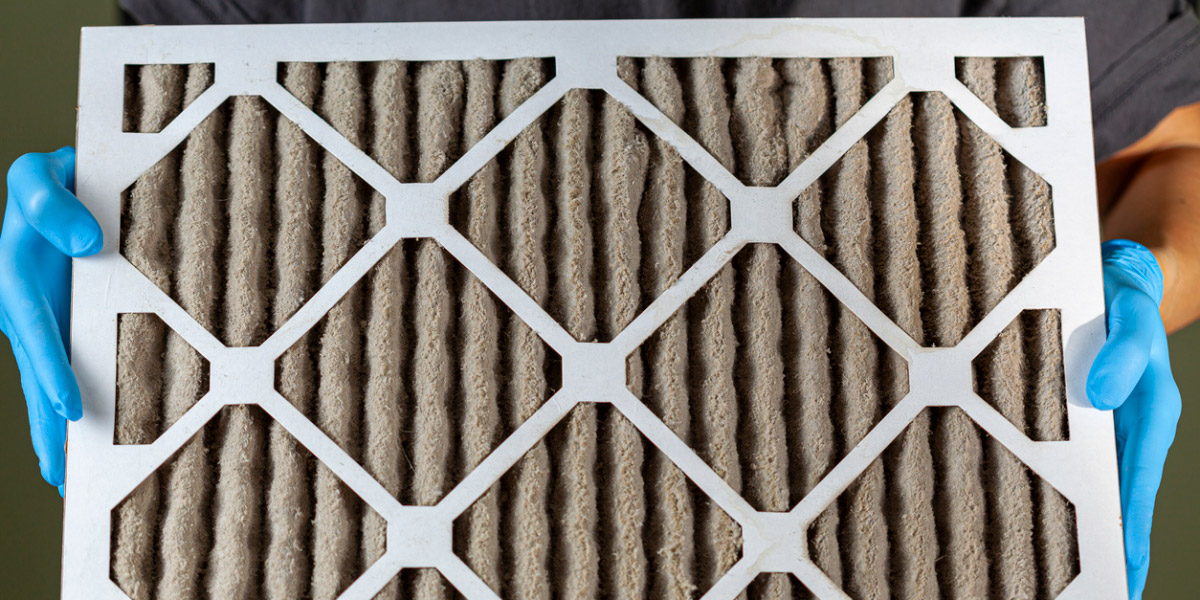 A person wearing blue gloves is holding a heavily clogged dirty air filter in hands before replacing it with the new one. Paper based, card board frame plated filters are used in hvac, ac , furnaces.