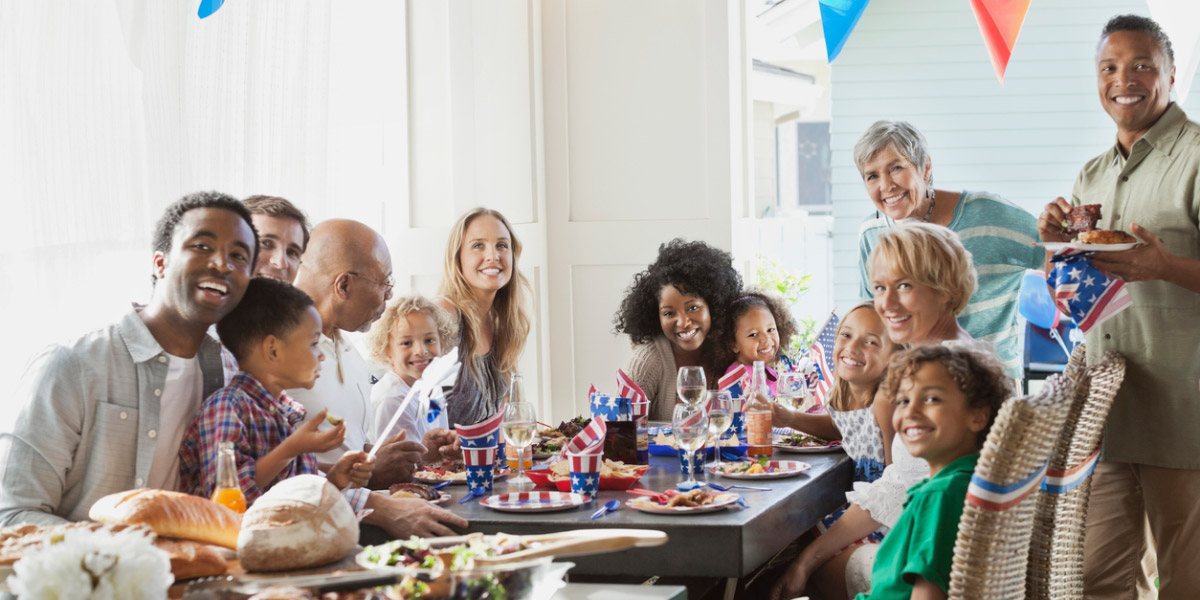 Portrait of happy multi-ethnic family and friends at dining table celebrating Independence Day.