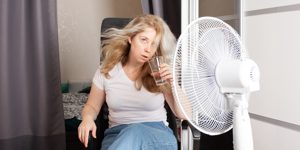 Tired woman seeking relief from high temperatures, trying to cool down in a non-air-conditioned room, Summer heat.