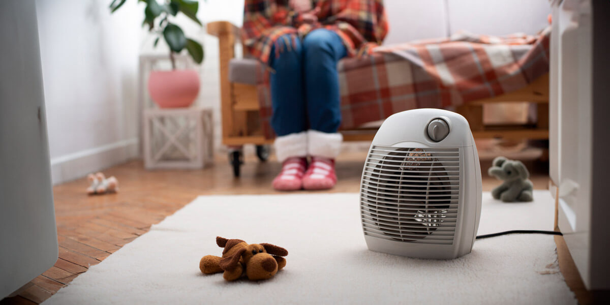A woman sits on the floor next to a heater, seeking warmth and comfort in a cozy setting.